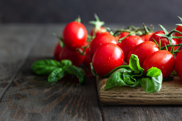 Fresh ripe cherry tomatoes and basil on a wooden background.