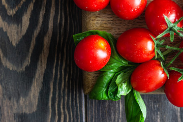Fresh ripe cherry tomatoes and basil on a wooden background.