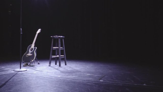 Guitar, microphone and chair on empty stage awaits for artist in the dark