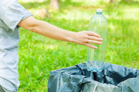 Woman throwing empty plastic water bottle in garbage bin in the park