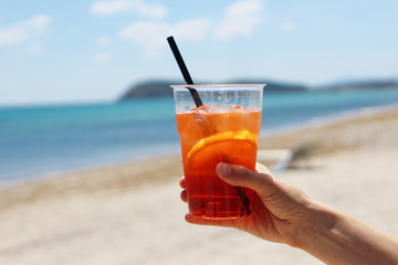 Closeup of womans hand holding chilled aperol coctail with orange slice, drinking straw and ice...