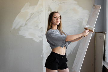 A young girl stands on the background of a putty wall. She holds a construction brush in her hand