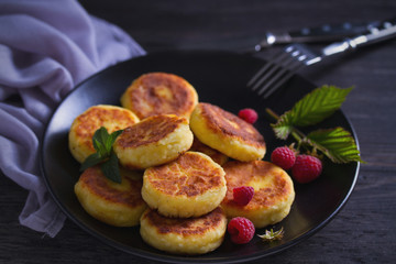 Cottage cheese pancakes on black plate. Syrniki and raspberries
