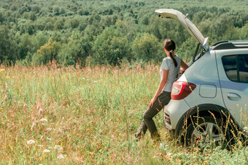 Woman traveler sitting on hatchback car with forest background