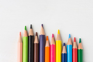 Row of multicolored rainbow palette pencils on white wood background. School art education kids creativity concept. Poster banner template with copy space