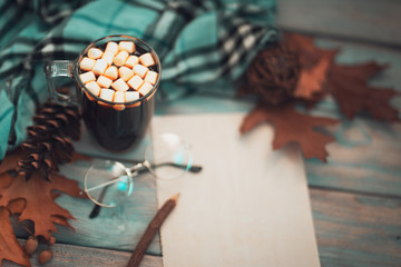Flatlay composition with white knitted scarf, cup of coffee, firewood, letter, blank paper card, glasses on wooden desk table. Hygge style, cozy autumn or winter concept. Overhead, toned background
