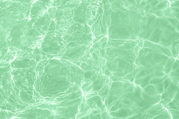 Closeup of calm clear water surface with water splashes in trendy neo mint color. Swimming pool...