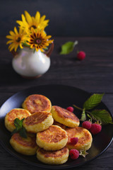 Cottage cheese pancakes on black plate. Syrniki and raspberries
