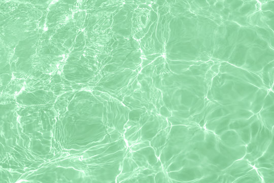 Closeup of calm clear water surface with water splashes in trendy neo mint color. Swimming pool water texture. Trendy fresh abstract nature background. Year color trend concept.