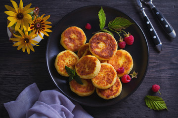 Cottage cheese pancakes on black plate. Syrniki and raspberries