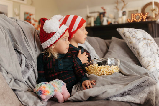 A young brother and sister eating popcorn and watching a movie at christmas time