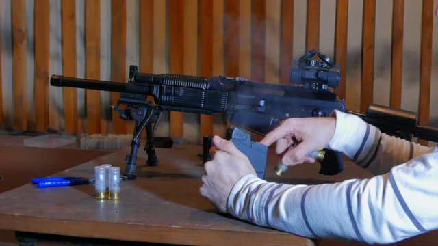 The shooter releases smoke from the magazine after the shooting and loading it with cartridges. A man trains in target shooting in an indoor shooting range using a high-caliber semi-automatic carbine 