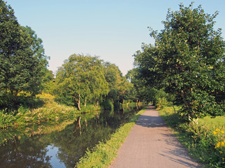 Fototapeta na wymiar a long straight path along a canal in summer with trees reflected in the water in bright summer sunlight near luddenden in west yorkshire
