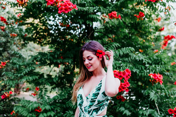 portrait of beautiful blonde young woman smiling at sunset. Playing with red flowers. Happiness and lifestyle concept outdoors