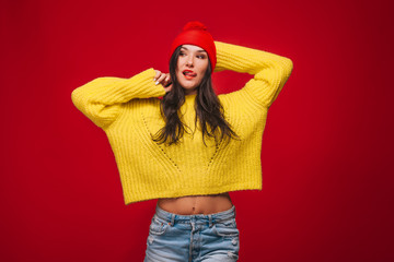 girl in a yellow sweater and a hat on a red background holding her head and grimacing