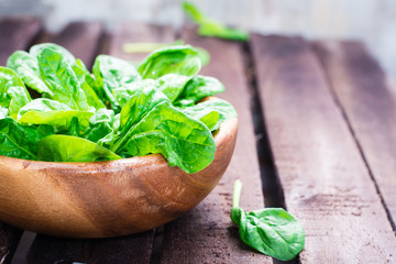 Fresh baby spinach leaves in a bowl on a wooden table. Close-up of herbes
