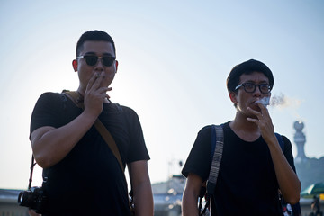 Asian young man wearing sunglasses smoking a cigarette at the music festival scene