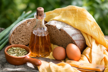 Home-made fresh bread, bottle with sunflower oil, pumpkin sunflower seeds, green onions, a knife and eggs, on an old wooden board. 