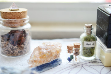 Fototapeta na wymiar Mystical Peridot in a vial, healing crystals set up on a white cloth. Azurite berries in miniature vial. Crystal display, bohemian decorations on a brightly lit background. Fresh and colorful crystals