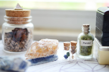 Mystical Peridot in a vial, healing crystals set up on a white cloth. Azurite berries in miniature vial. Crystal display, bohemian decorations on a brightly lit background. Fresh and colorful crystals