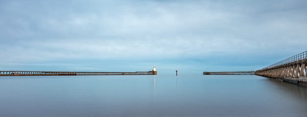 A boardwalk and jetty with lighthouse in a calm sea.