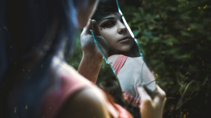 A girl holding a mirror which depicts feminine demon with black eyes. Format 16:9 (film frame).