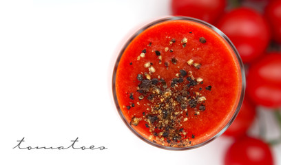 Glass cup with tomato juice with ground black pepper and cherry tomatoes on white background. top view