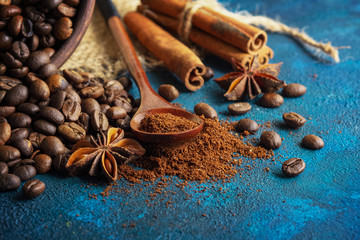 Fototapeta na wymiar coffee grains scattered on a blue textural background, anise stars, cinnamon sticks and ground coffee in a wooden spoon.