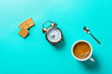 Cup of freshly brewed coffee with crema home baked bran cookies alarm clock spoon on turquoise background. Breakfast morning energy concept flat lay with copy space