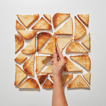 The hand of the girl makes a pattern of square-shaped pieces of fried toast on a gray background. Flat lay