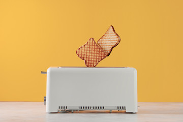 Roasted toast bread popping up of toaster with yellow wall