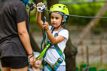 Fototapeta na wymiar Happy school girl enjoying activity in a climbing adventure park on a summer day