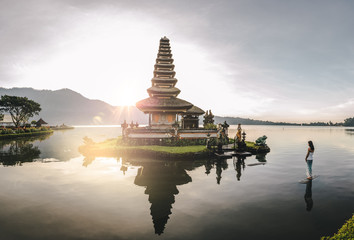 beautiful woman standing in a lake looking at a balinese water temple at sunrise
