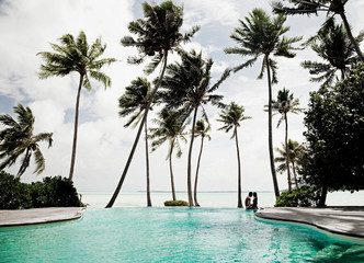 Couple sitting on edge of pool at luxury tropical resort on the beach