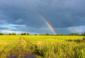 Rural landscape with dirt road and rainbow in the sky after the rain.