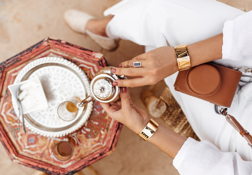 Female hands with rings and bracelets holding a pot of tea