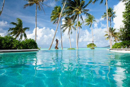 Woman walking by infinity pool on vacation at luxury resort