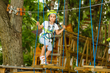 Adorable little girl enjoying her time in climbing adventure park on warm and sunny summer day. Summer activities for young kids. Child having fun on school vacations.