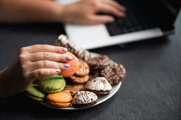 Unhealthy snack at work time. Woman eating cookies at workplace. High calorie, fattening junk food, weight gain