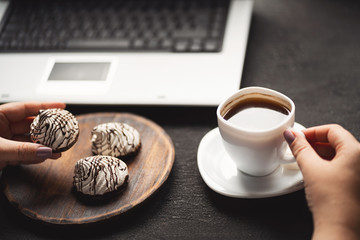 Unhealthy snack at work time. Woman eating chocolate cookies and drinking coffee at workplace. High calorie, fattening junk food, weight gain