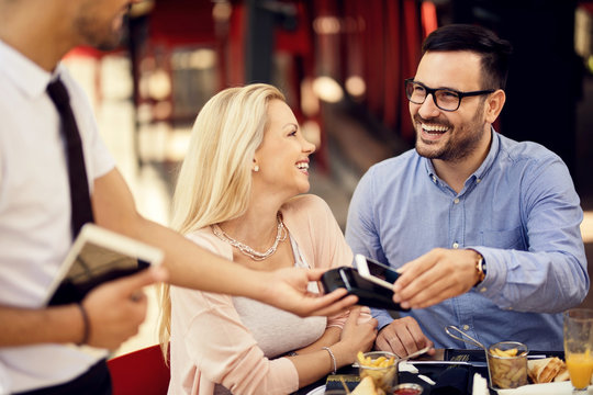 Happy man using mobile phone for contactless payment in a restaurant.