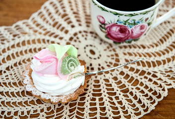 cake with cream, a cup of black coffee and a silver spoon on a napkin. delicious dessert