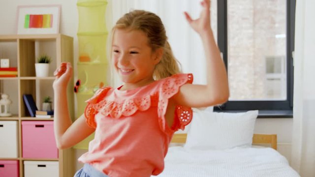 childhood and leisure concept - happy little girl dancing in her room at home