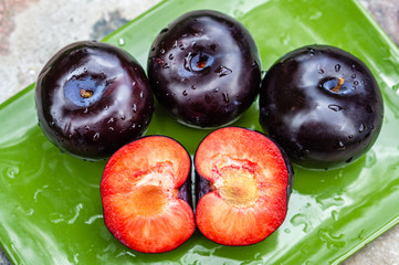 Three dark purple plum fruits and one cut on a green plate