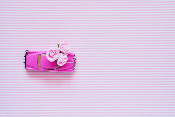 Riga, Latvia - July 28, 2019. Pink retro toy car delivering pink flowers bouquet on pink background. Top view, copy space. Flowers delivery. Greeting card