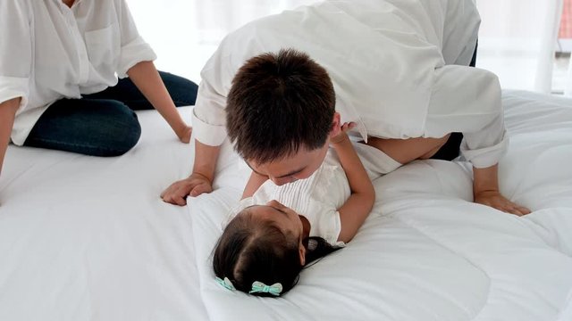 Asian family happy spending time together in the house. Father kissing daughter aged three and enjoying playing on the bed. Happiness in the home. Slow motion
