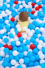A little baby playing in kids pool full of plastic balls