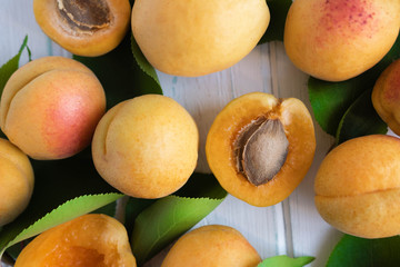 Ripe apricot fruit with green leaves close-up on a light wooden background. Summer fruit containing pectin.