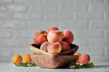 Peaches in wooden bowl with white brick wall background