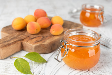 Jars with apricot jam on white wooden background